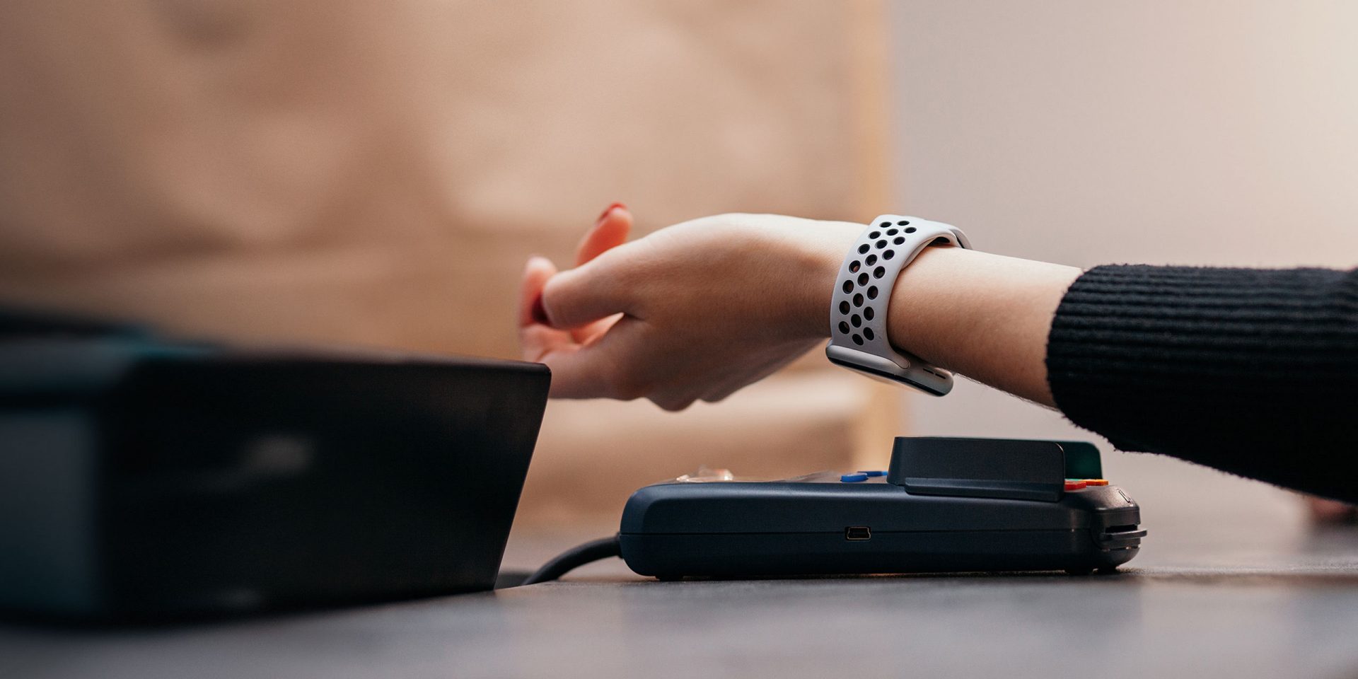 Nahaufnahme einer Hand mit Smartwatch, die an ein Lesegerät gehalten wird, um einen Bezahlvorgang mit Apple Pay durchzuführen.