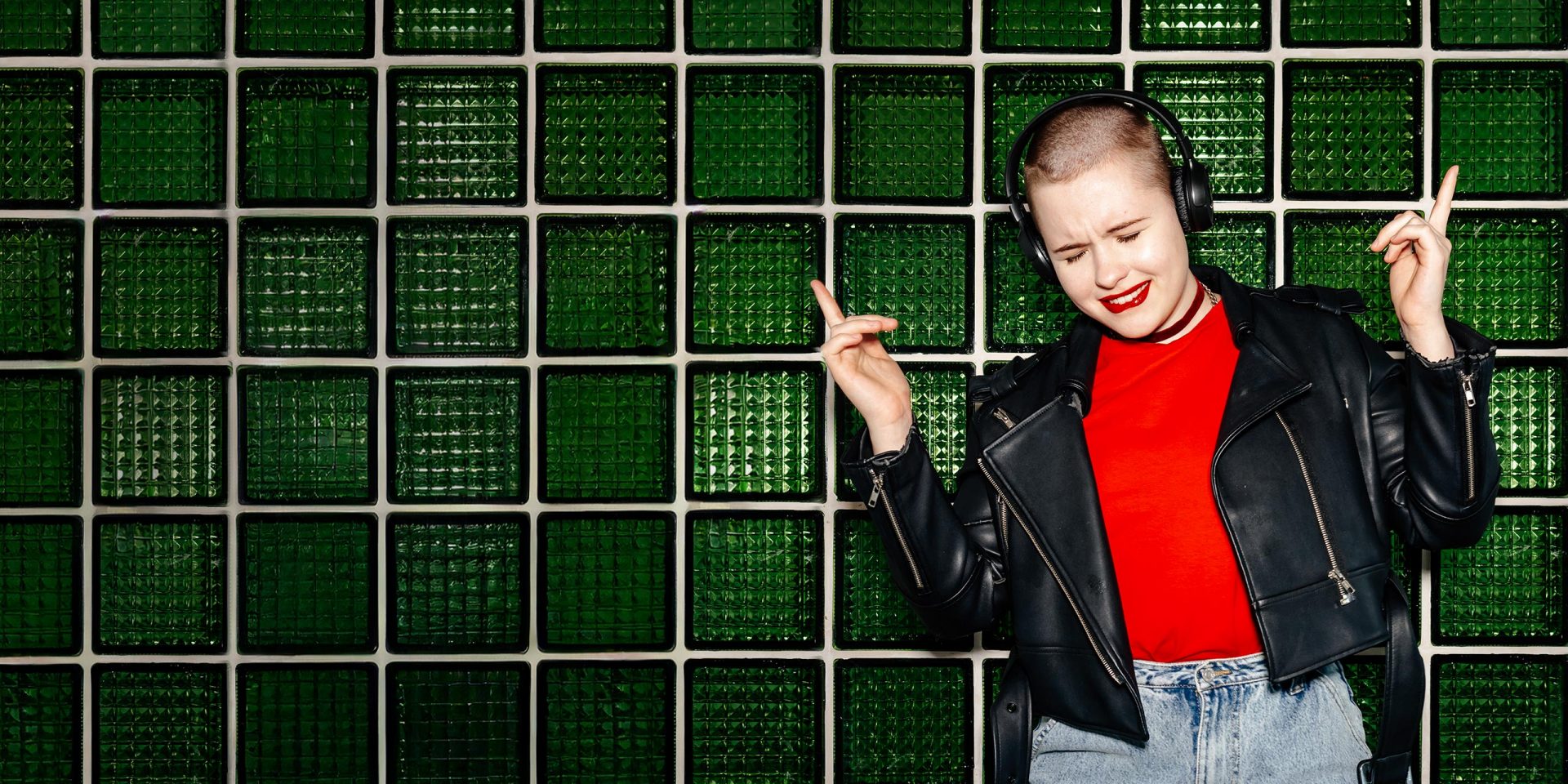 Junge Frau mit Kopfhörern tanzt vor grüner Wand. Symbolbild für "Barrierefreiheit".