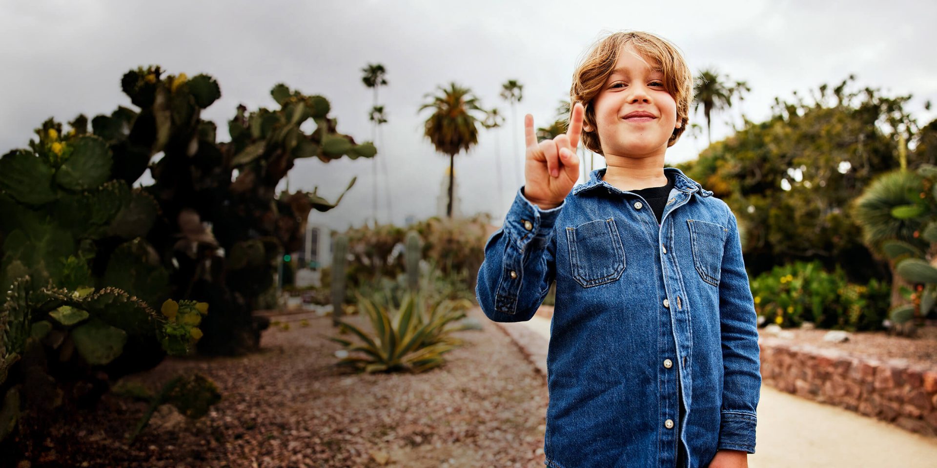 Porträt eines lächelnden Jungen, der im Park steht und das Hornzeichen macht. Symbolbild für "bestsign einrichten".