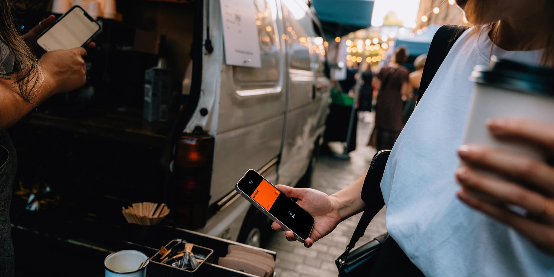 Junge Frau bezahlt kontaktlos mit ihrem Smartphone an einem Kaffeemobil, sie nutzt ihre kostenlose Kreditkarte