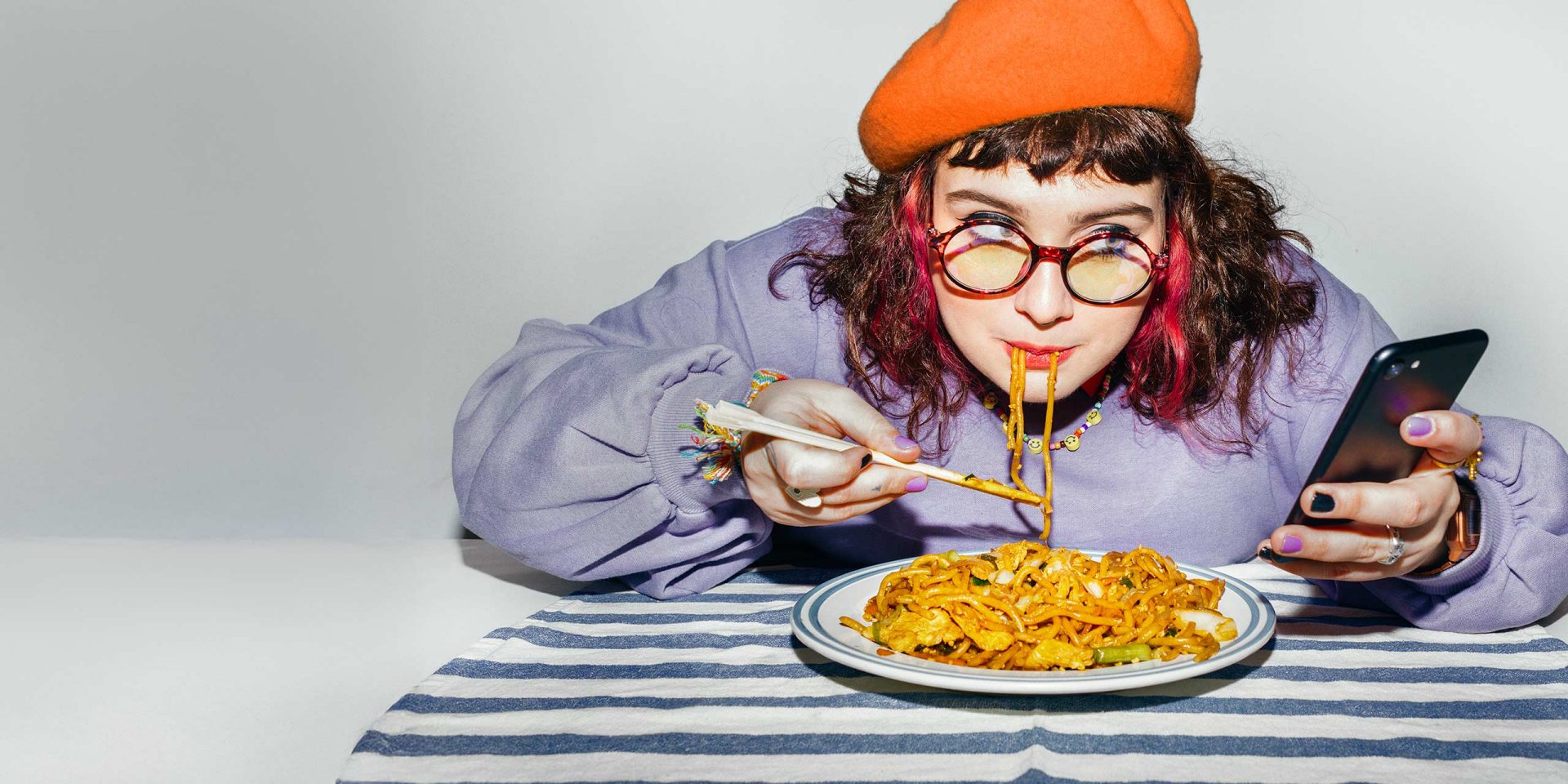 Eine junge Frau checkt beim Essen den norisbank FinanzPlaner auf ihrem Handy.