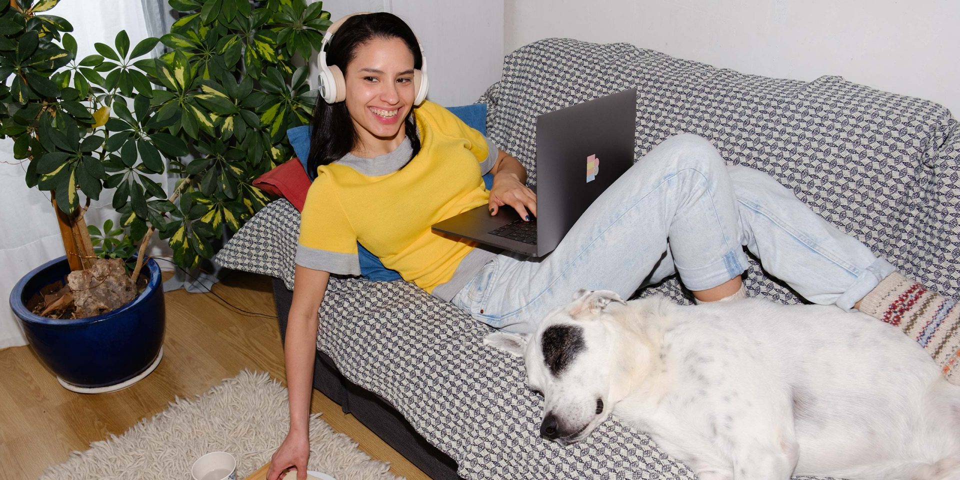 Junge Frau liegt mit ihrem Hund auf dem Sofa und macht Online-Banking. Symbolbild für "Girokonto plus".