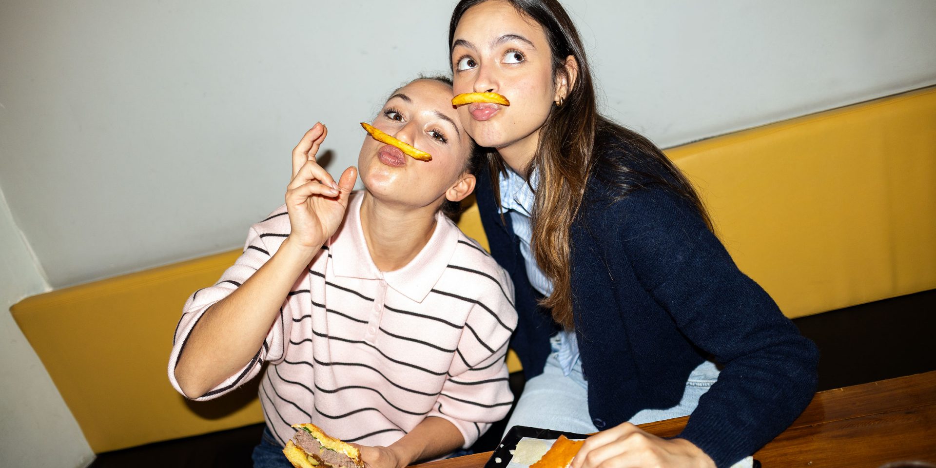 Symbolbild für "Girokonto Vergleich": Junge Freundinnen, die spielerisch mit Pommes Frites vor der Nase posieren und einen lustigen, leichten Moment in einem Restaurant teilen