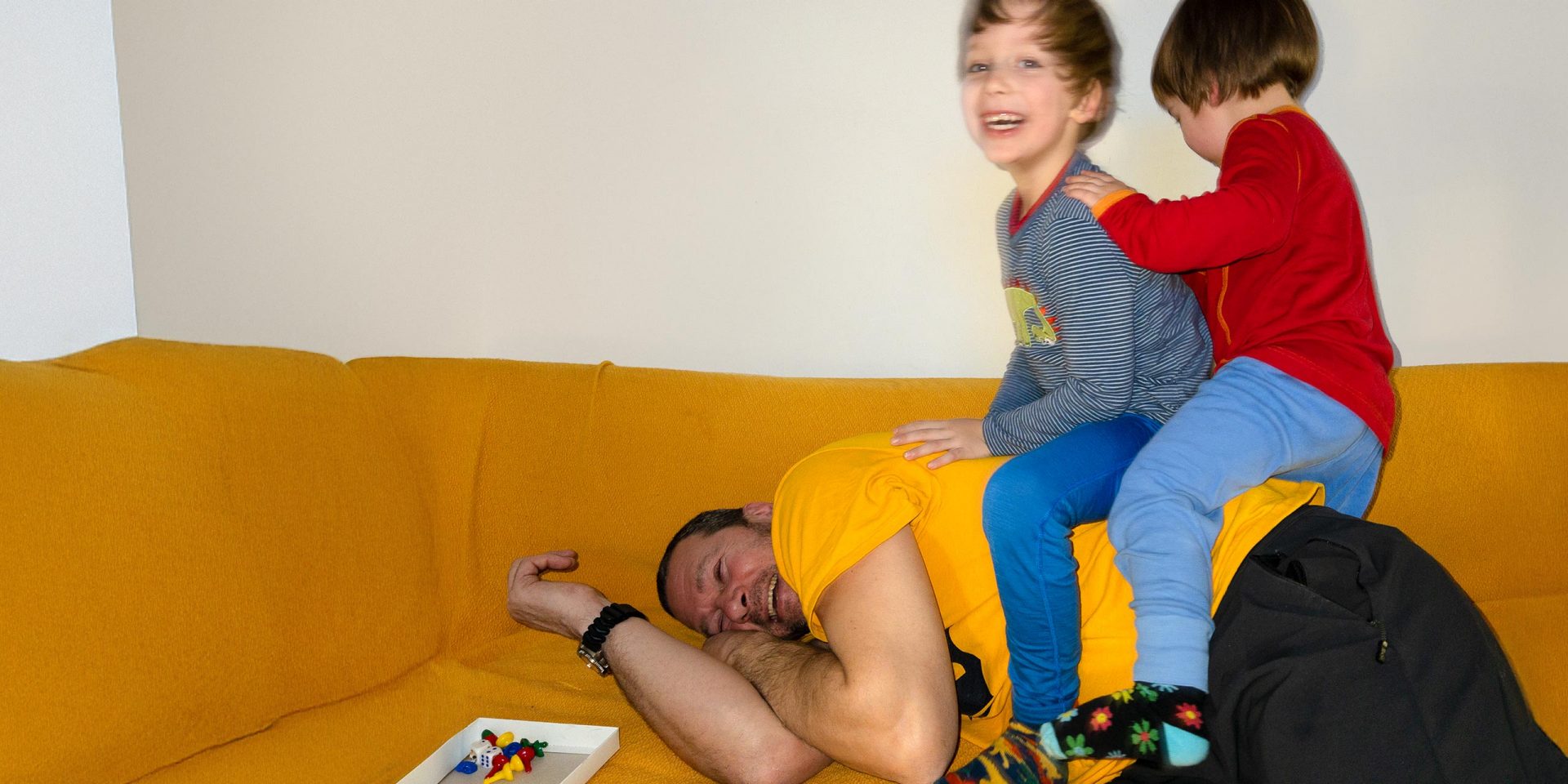 Kinder toben mit ihrem Papa auf dem Sofa. Symbolbild für "Kindergeld".