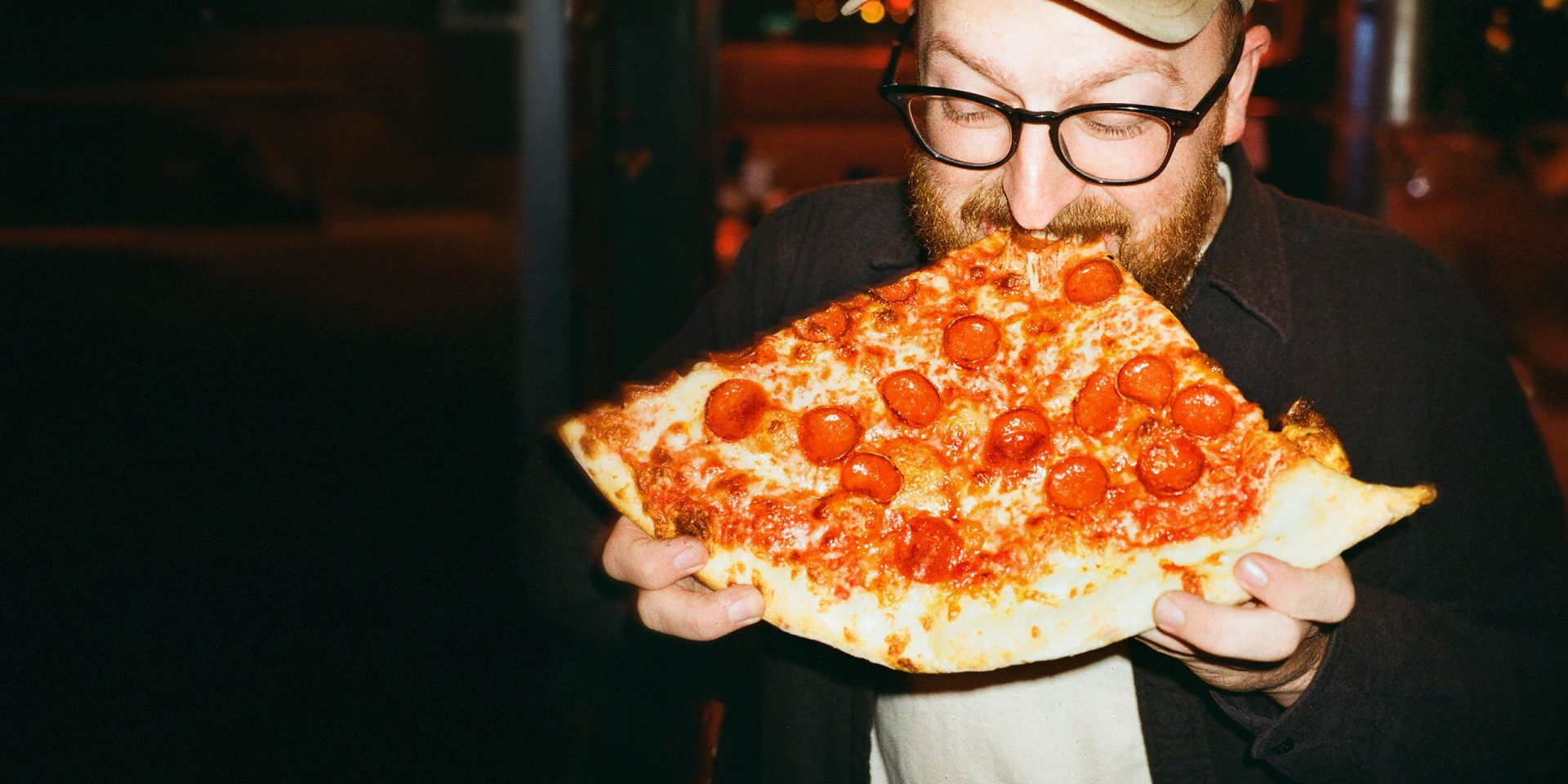 Ein Mann beißt in ein riesiges Stück Pizza – passend zum Thema Kredit erhöhen, wenn der Appetit auf mehr finanziellen Spielraum wächst.