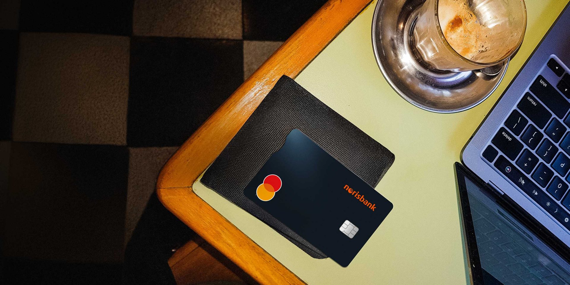 Eine Kreditkarte liegt auf einem Tisch neben einer Kaffeetasse und einem offenen Laptop.