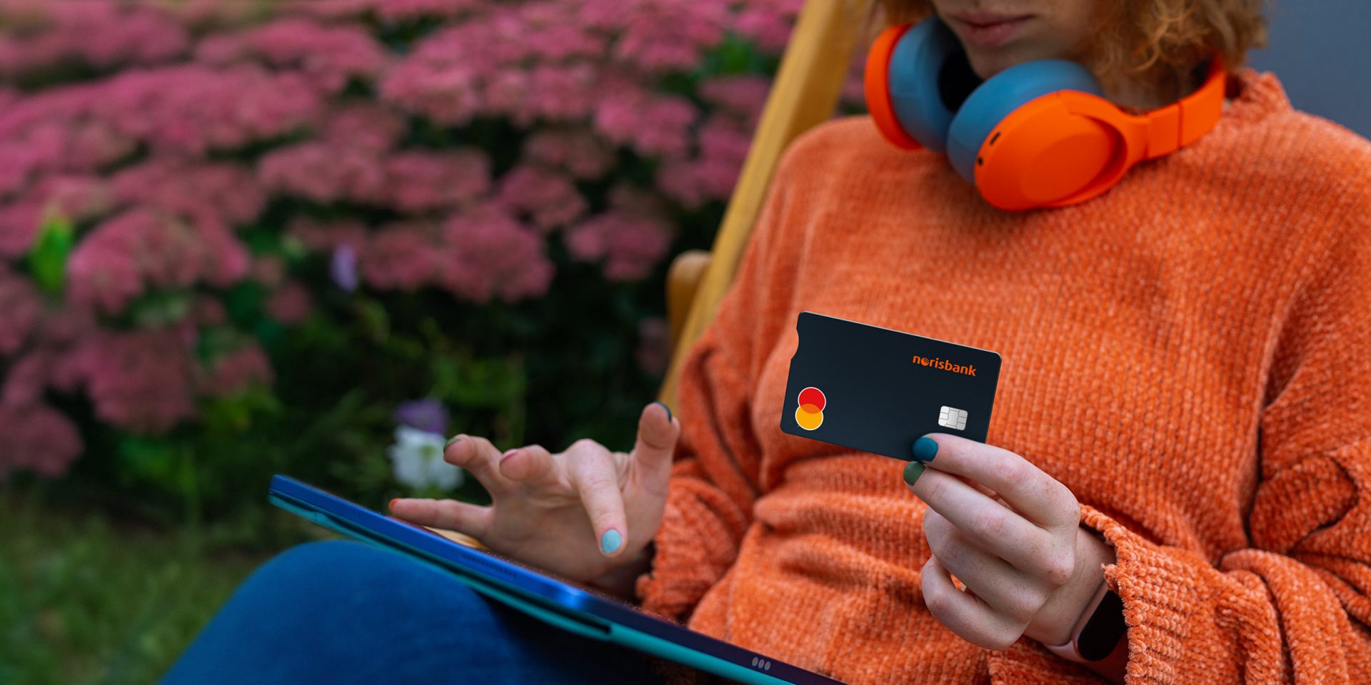 Eine Person scrollt auf ihrem Tablet und hält die norisbank Mastercard Kreditkarte in der Hand.