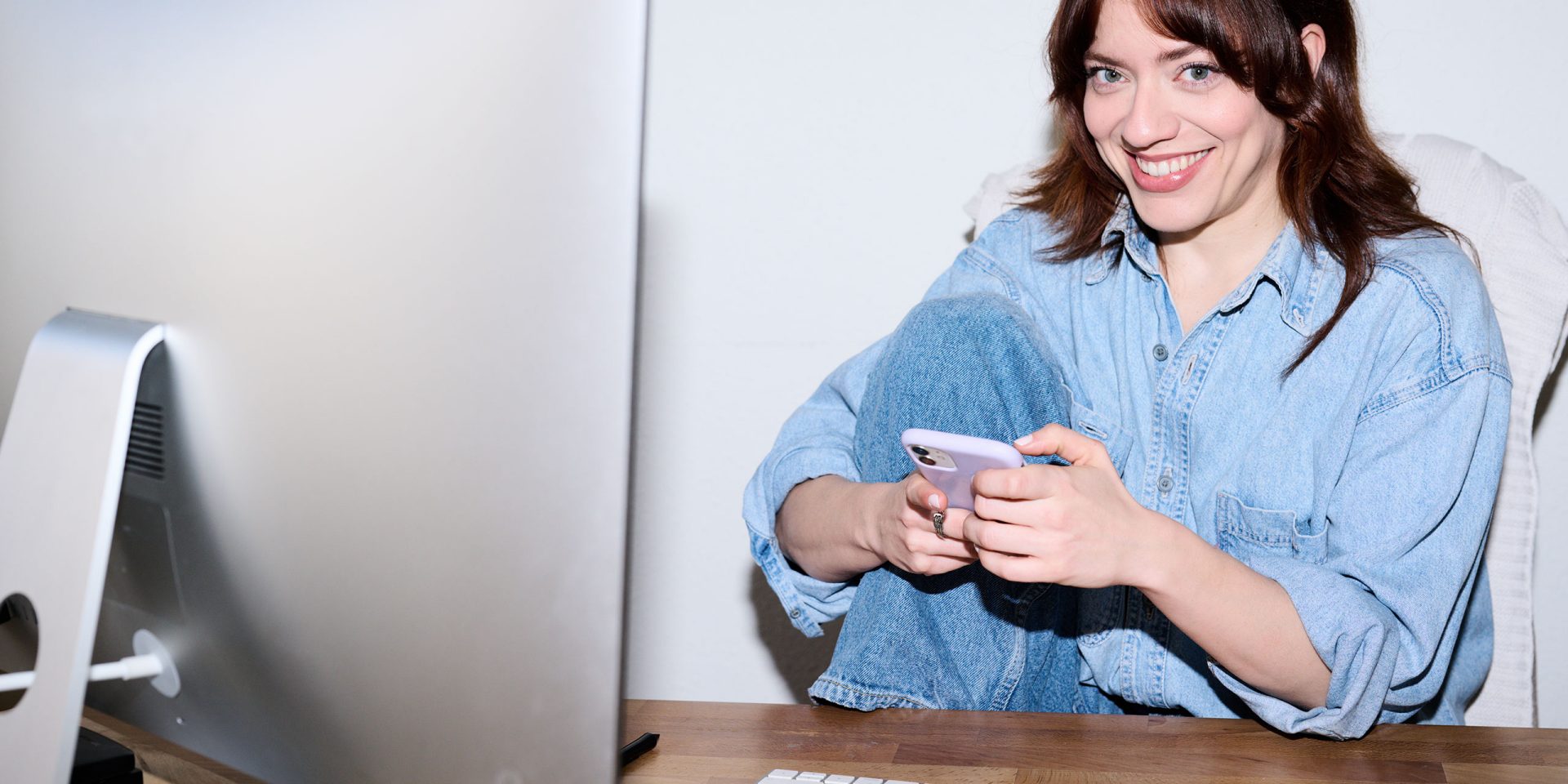 Sicheres online banking: Frau nutzt ein rosa Smartphone am Schreibtisch vor Computer