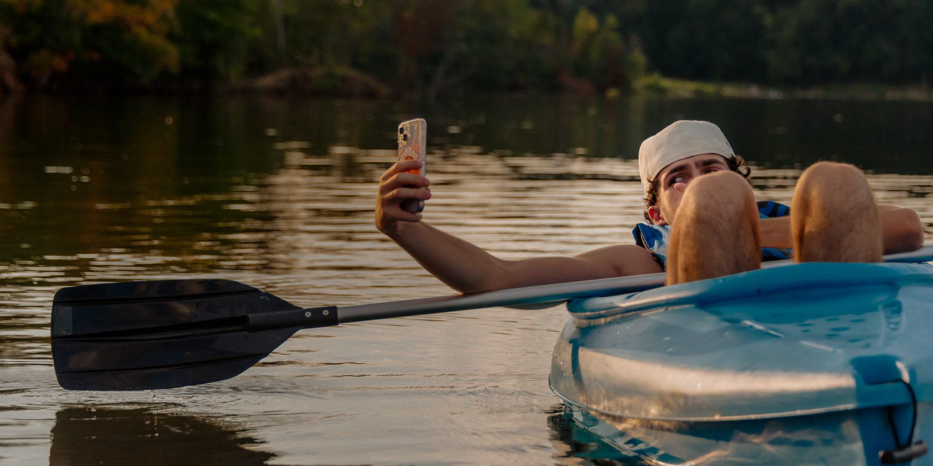 Eine Überweisung kann überall erledigt werden: Ein junger Mann liegt in einem Paddelboot und überweist mit der SEPA Echtzeitüberweisung Geld über sein Handy.
