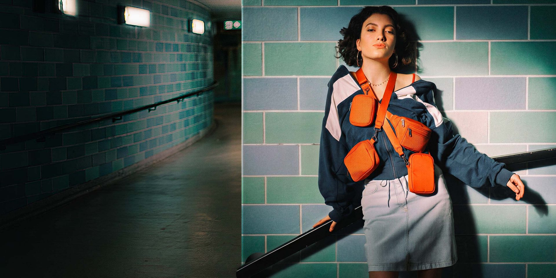 Die Frau lehnt im Kacheltunnel mit mehreren orangefarbenen Taschen: eine visuelle Metapher für strukturierte Organisation, wie bei norisbank Unterkonto.