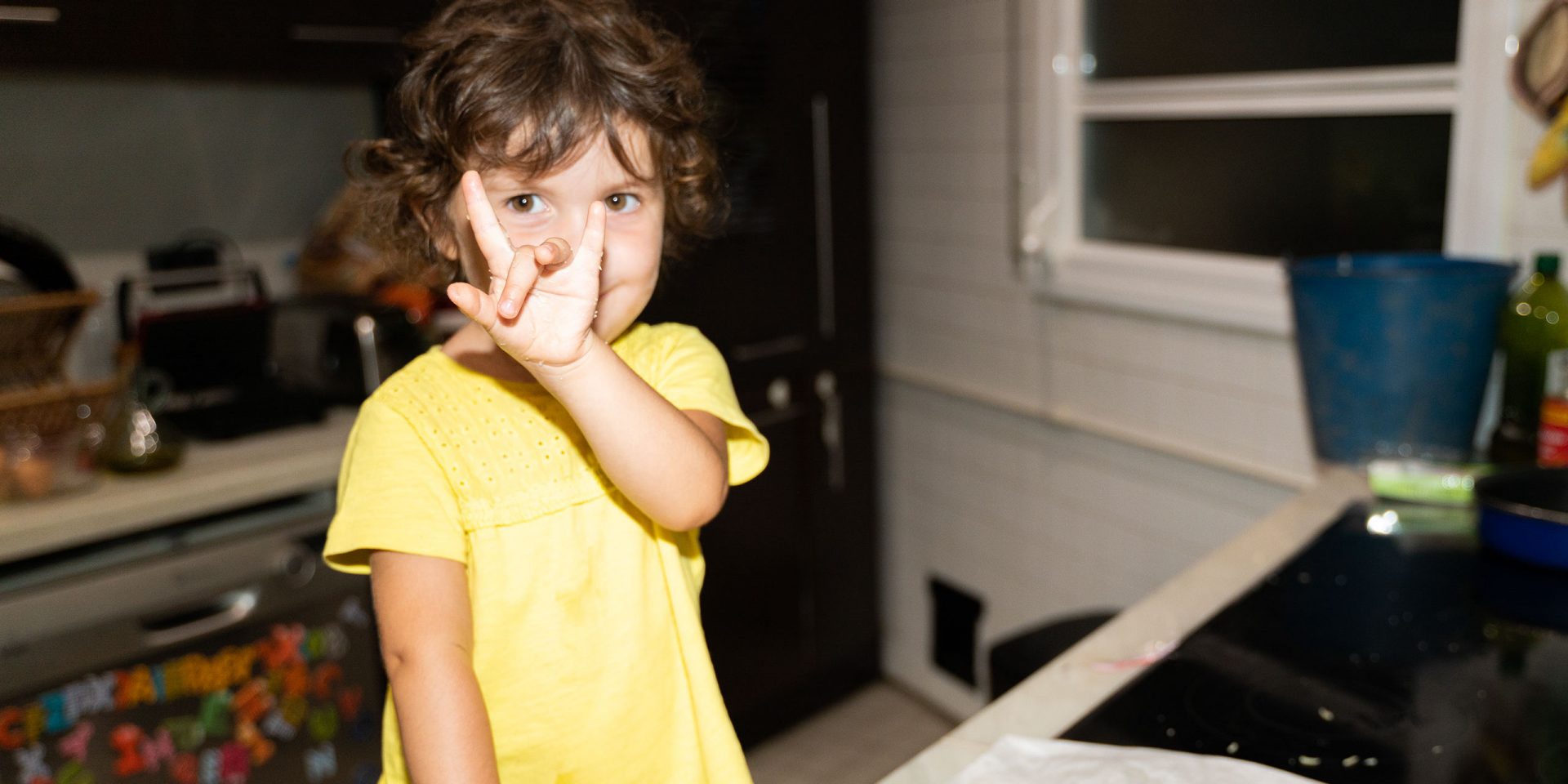 Kind am Küchentisch zeigt das Horn-Zeichen. Symbolbild für "Sparen für Kinder"