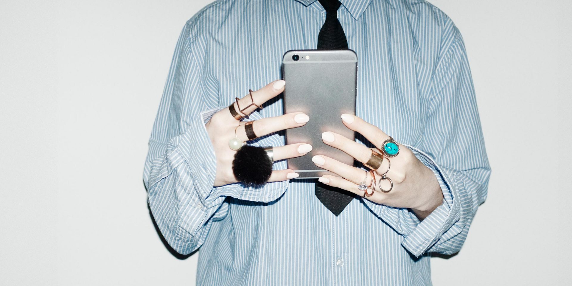 Nahaufnahme von Händen mit auffälligen Ringen, die ein Smartphone halten. Symbolbild für "Tagesgeldzinsen"