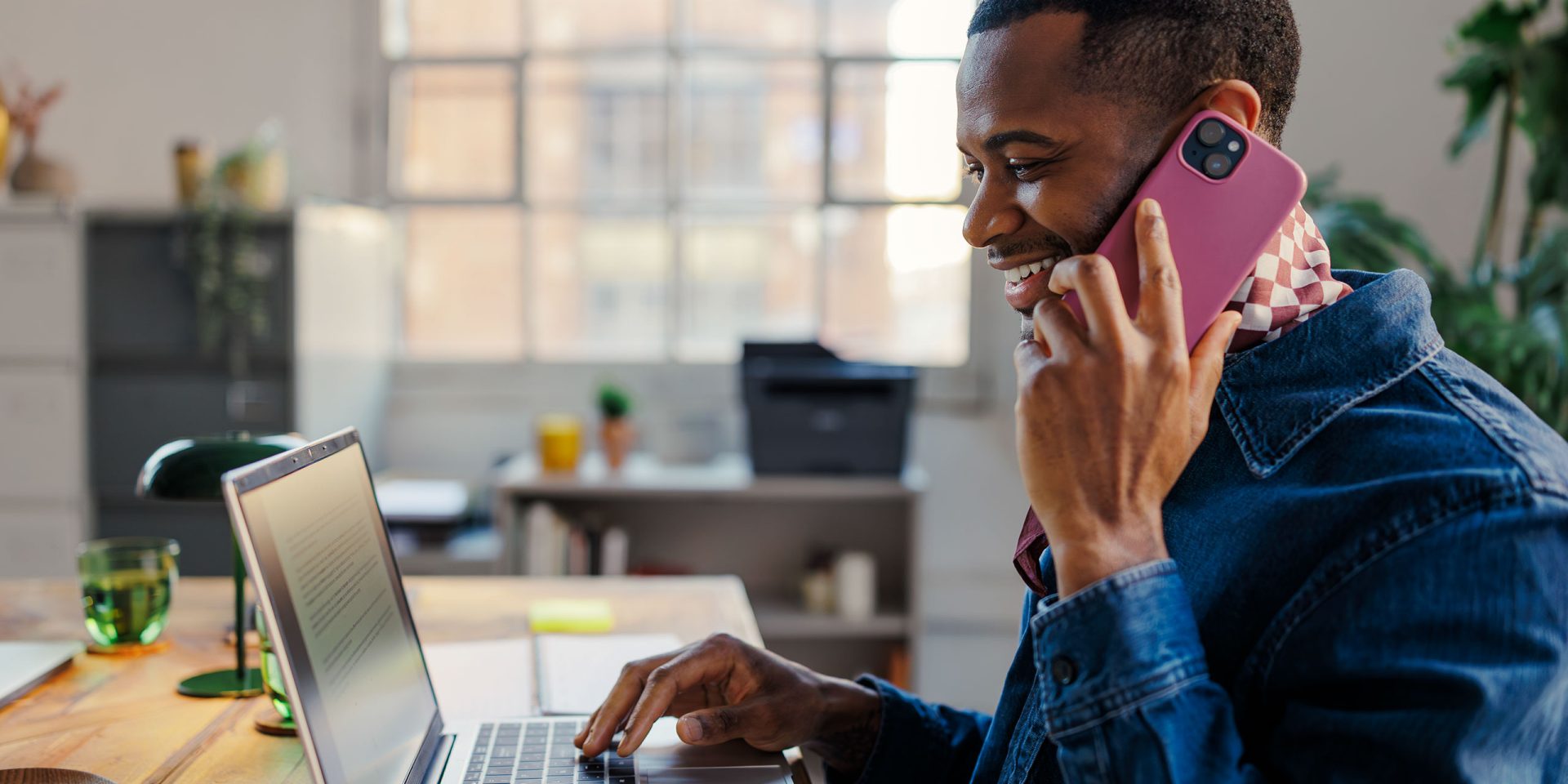 Ein Mann sitzt am Schreibtisch und schaut in seinen Laptop, während er per Telefon-Banking Bankgeschäfte durchführt.