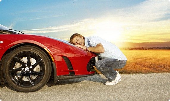 Mann lehnt seinen Kopf glücklich auf sein Auto, dass er sich mit einem Online-Kredit finanziert hat