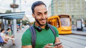 junger mann steht an der straßenbahnhaltestelle und liest auf seinem smartphone das neueste finanzwissen-thema der norisbank